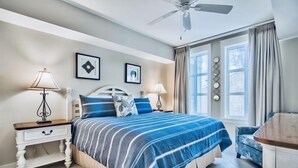 Un dormitorio con una cama, dos mesitas de noche, un ventilador de techo y una ventana con cortinas.