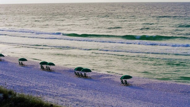 Una playa con filas de sillas y sombrillas, una orilla arenosa y olas acercándose a la costa.