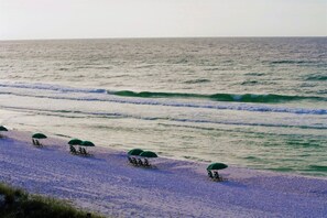 Een strand met rijen ligbedden en parasols, een zandstrand en golven die de kust naderen.