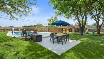 Enjoy a refreshing swim in the backyard pool surrounded by lush greenery and shaded seating.