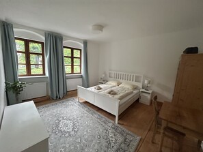 Ein Schlafzimmer mit Bett, Nachttischen, Schreibtisch und einem Fenster mit Vorhängen.