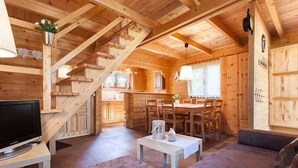 L'intérieur d'un chalet en bois comprend un coin repas, un canapé et un téléviseur.