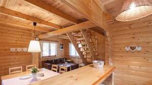 L'intérieur d'un chalet en bois comprend une table à manger, des chaises, un canapé, un escalier et un luminaire suspendu.