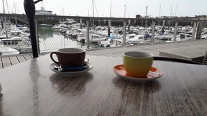 A table with two cups on a balcony overlooking a marina with boats.