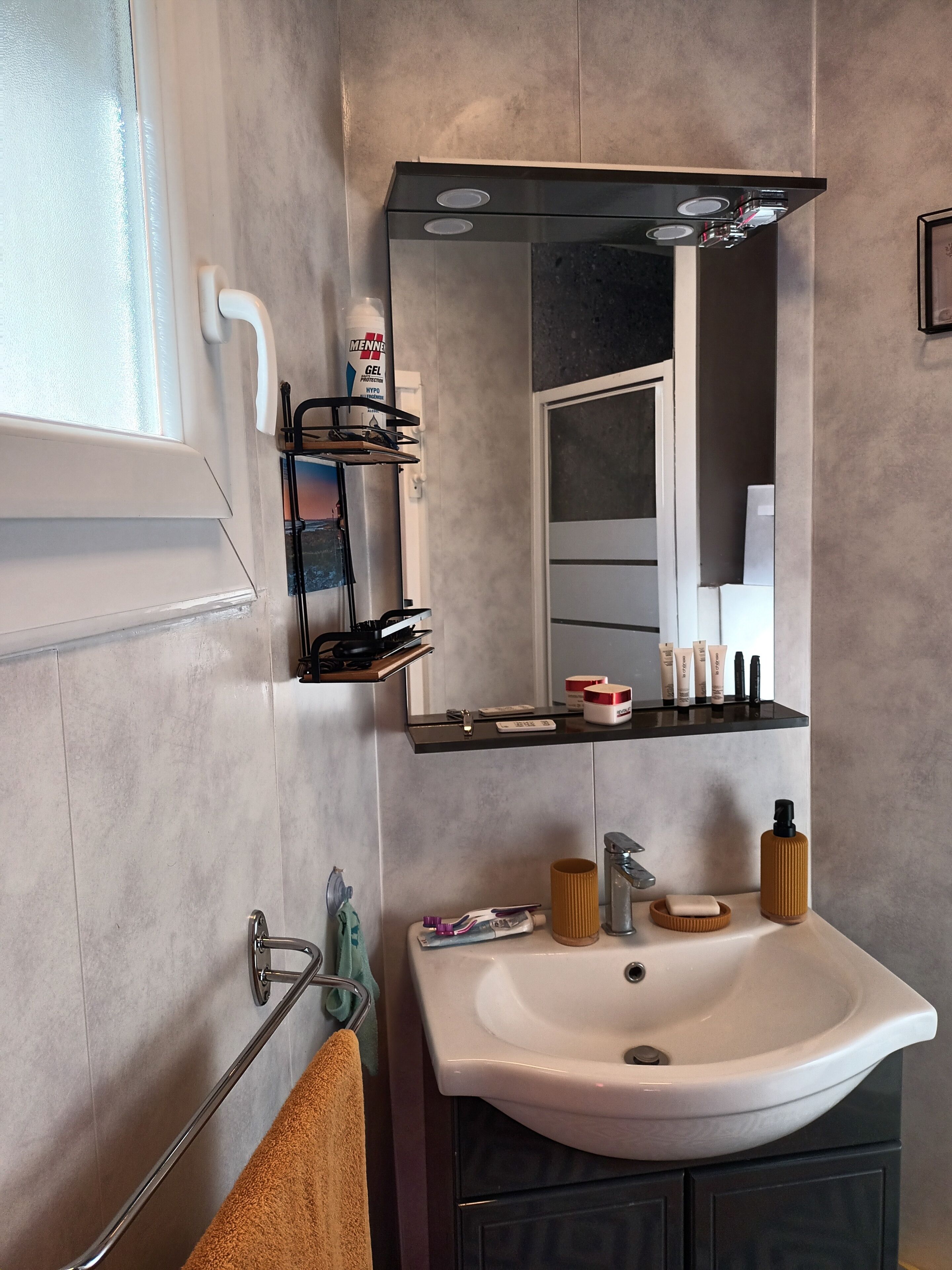 A modern bathroom with a white sink, a mirror, and a shelf with toiletries.