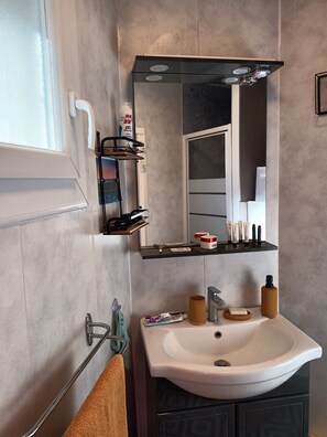 A modern bathroom with a white sink, a mirror, and a shelf with toiletries.