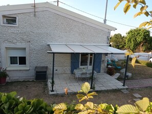 A house with a stone exterior, a covered patio with a table and chairs, and a small garden area.