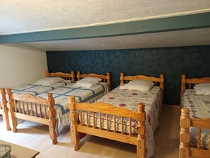 A room with four wooden beds arranged in a row, each with a wooden headboard and a floral-patterned bedspread. The room has a sloped ceiling and a dark blue wall.