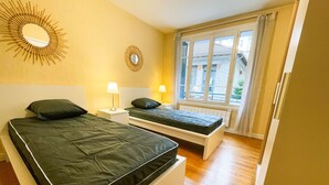 A bedroom with two beds, a large mirror, and a window with a view of buildings. - #FL | The Harmony of Eras 🕊️ - T2 - Calm (Grenoble)