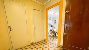 A hallway with a checkered floor, a wooden door, and a view into a dining area with a table and chairs. - #FL | The Harmony of Eras 🕊️ - T2 - Calm (Grenoble)
