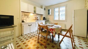 A compact kitchen with a dining area, featuring a checkered floor, white cabinets, and a dining table set for four. - #FL | The Harmony of Eras 🕊️ - T2 - Calm (Grenoble)