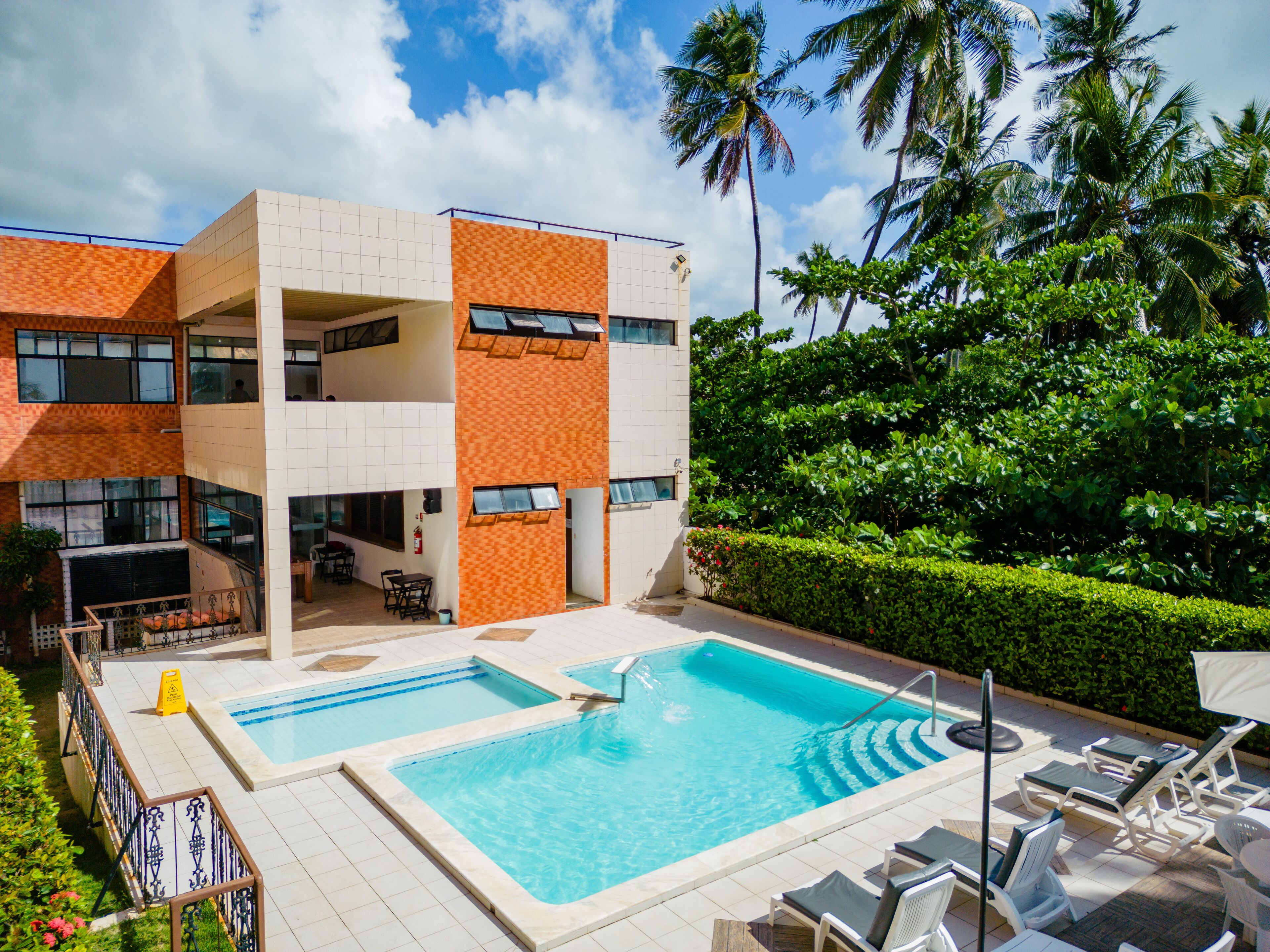 A modern hotel with a pool area, outdoor seating, and lush greenery.