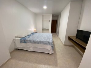 A bedroom with a bed, a bedside lamp, a TV on a stand, and a bathroom in the background.