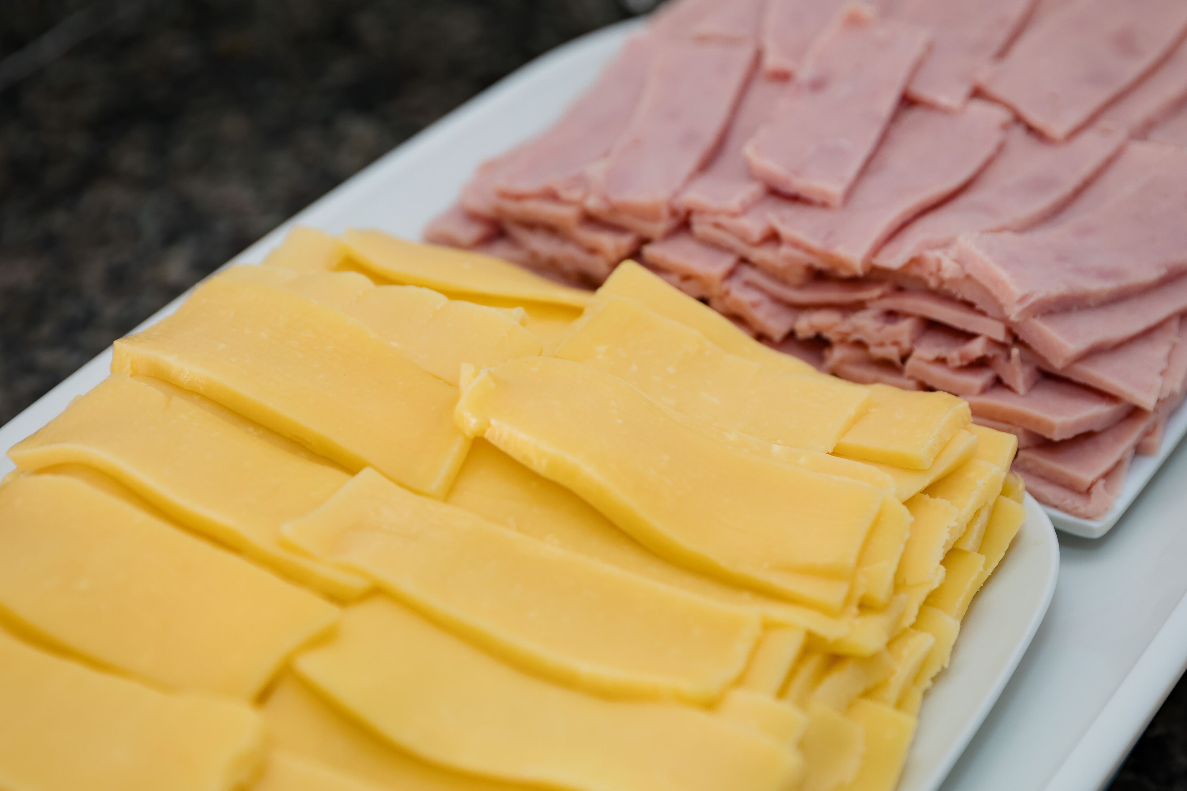 Un plato con queso amarillo en rodajas y jamón rosado.