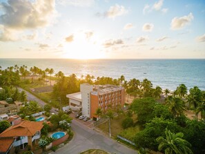 A hotel with a pool, surrounded by palm trees and a view of the ocean at sunset.