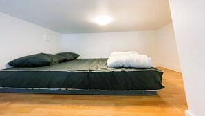 Una habitación pequeña con una cama individual, colchón, almohadas y una lámpara en el techo.
