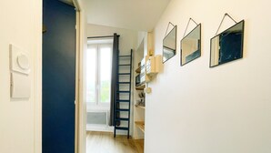 Un pasillo estrecho con una puerta azul, suelo de madera y un ventanal al final.