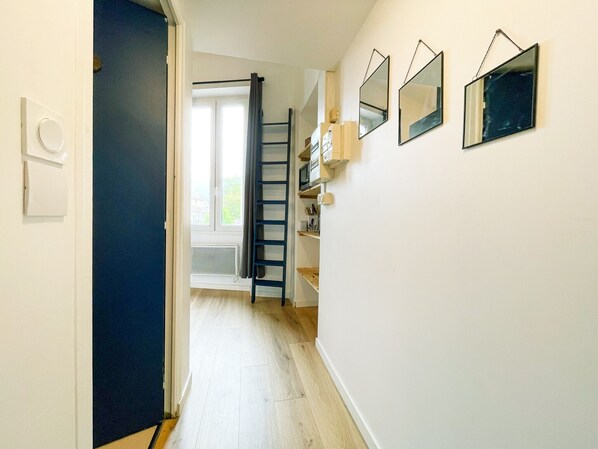 Un pasillo estrecho con una puerta azul, suelo de madera y un ventanal al final.