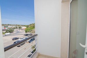 A balcony with a view of a parking lot and a road, a white wall, and a glass door.