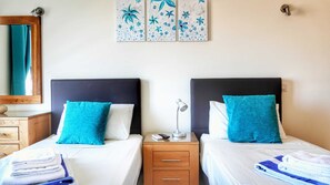 A hotel room with two beds, a nightstand with a lamp, a mirror, and a wall with floral artwork.