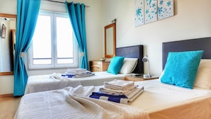 A hotel room with two beds, a bedside table with a lamp, a mirror, and a window with curtains. - Exquisite Apartment on the Lagos Marina - Marina Retreat (Lagos)