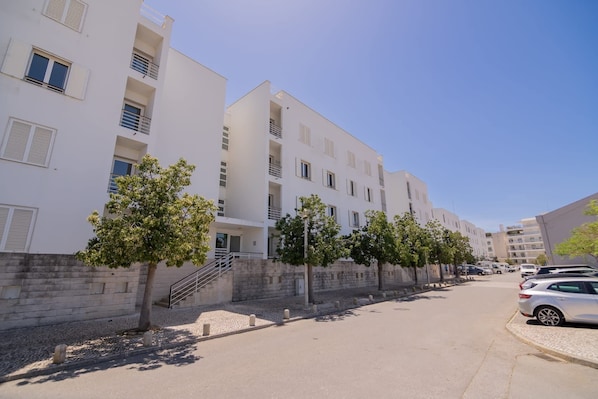 Une vue de rue d’un quartier résidentiel, avec des immeubles à plusieurs étages, un trottoir et des voitures garées.