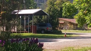 Un espacio exterior cubierto con un vehículo estacionado cerca, rodeado de vegetación y un paisaje montañoso.