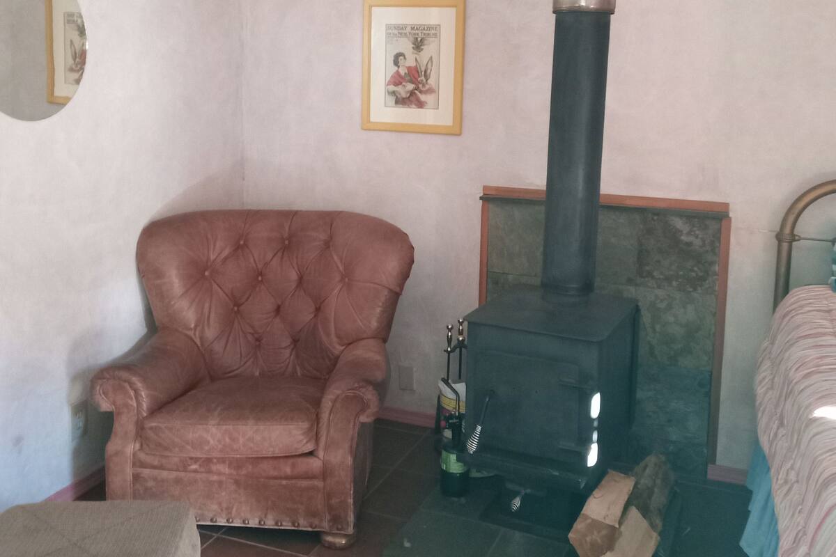 A cozy room with a brown leather armchair, a black wood-burning stove, and a framed picture on the wall.