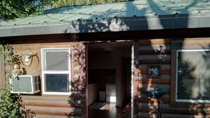 Una cabaña rústica con fachada de madera, un ventanal grande y una puerta que da a un espacio interior con cocina.