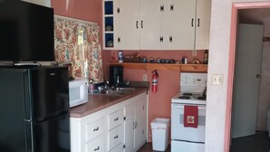 Cocina compacta con armarios blancos, un refrigerador negro, un microondas, una estufa y un lavamanos pequeño.
