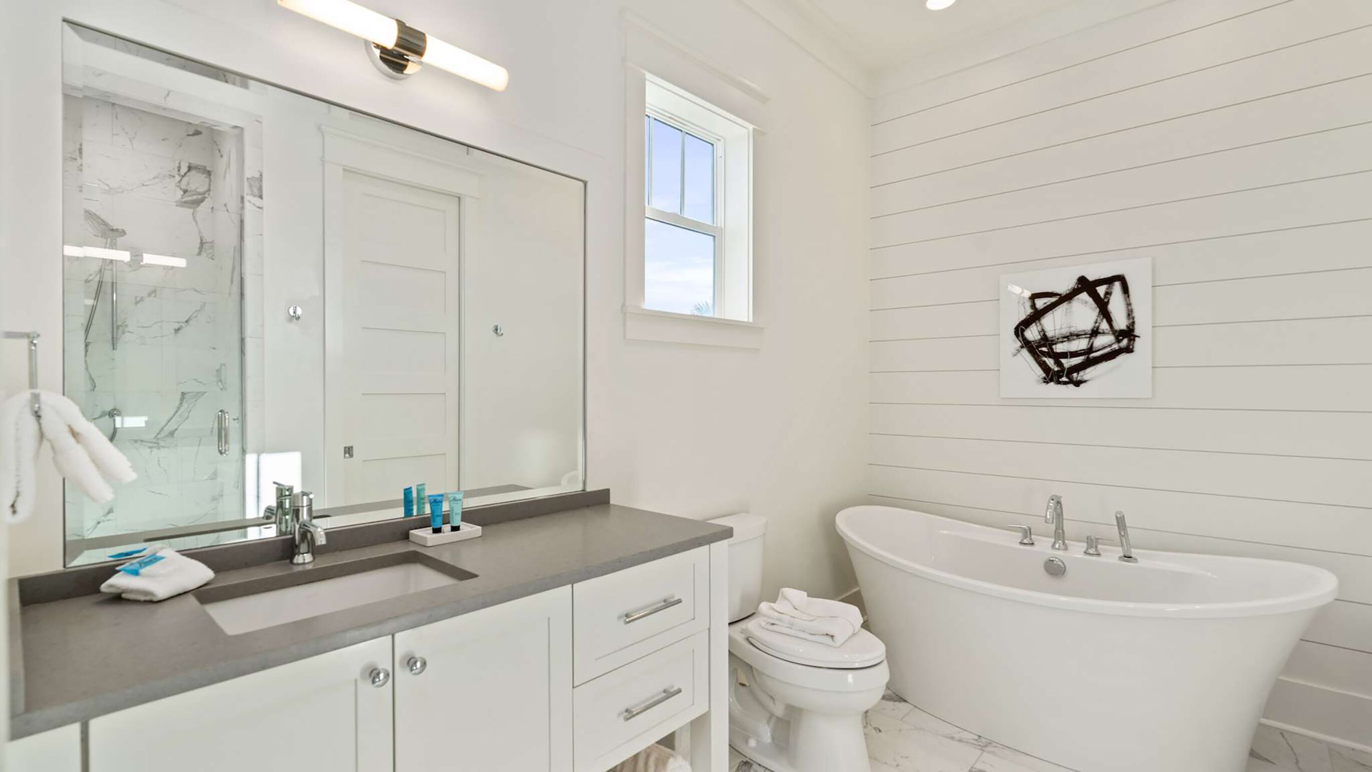 Une salle de bain moderne avec un grand miroir, une baignoire et des toilettes.