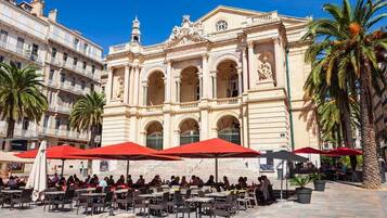 An outdoor café with tables and red umbrellas in front of a historic building with ornate architecture.