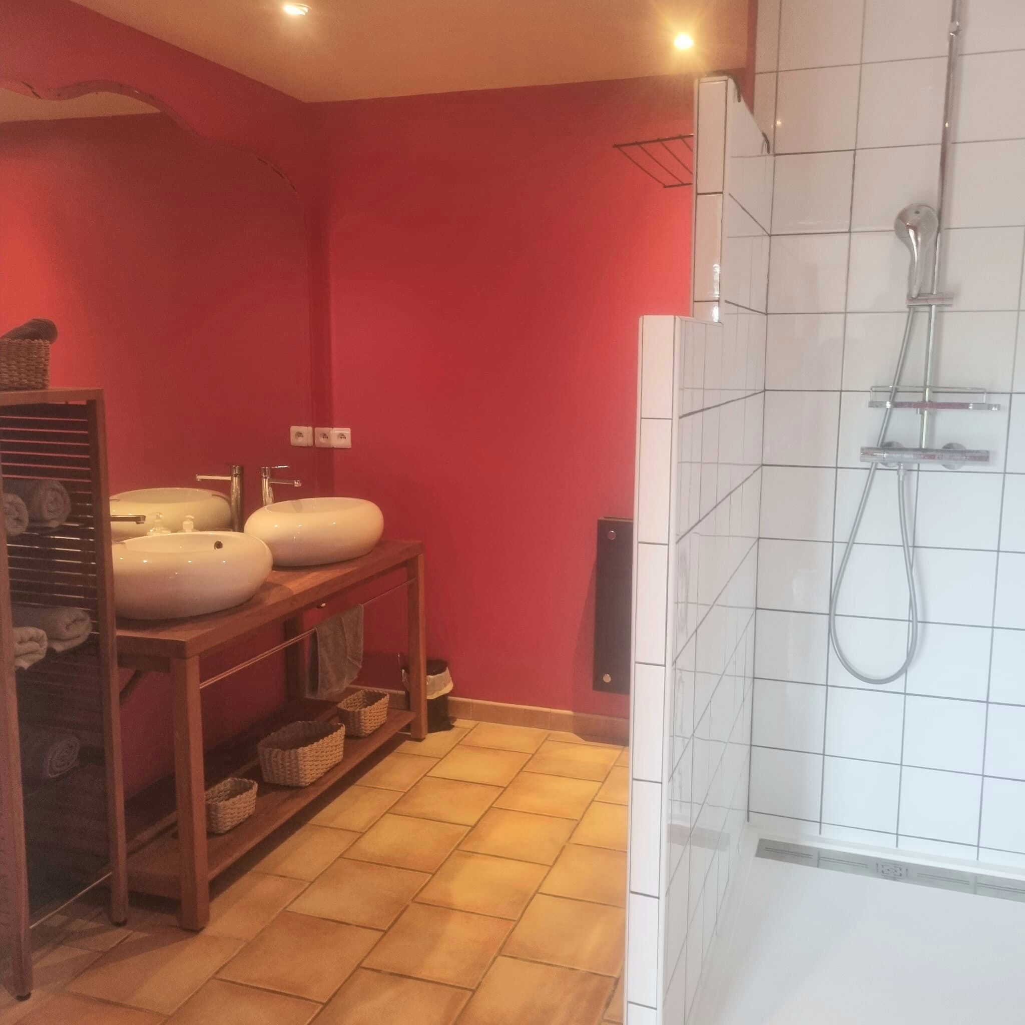 A bathroom with a wooden vanity, two sinks, a shower, and a tiled floor.