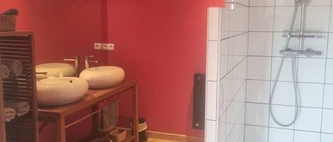 A bathroom with a wooden vanity, two sinks, a shower, and a tiled floor.