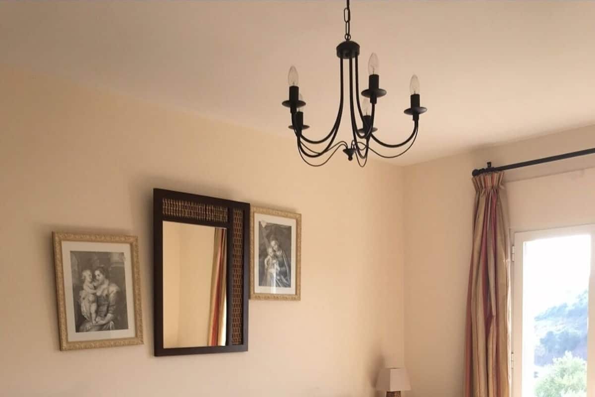 Ein Schlafzimmer mit einem großen Bett, zwei Nachttischen, einer Kristallleuchtre und gerahmten Bildern an der Wand.