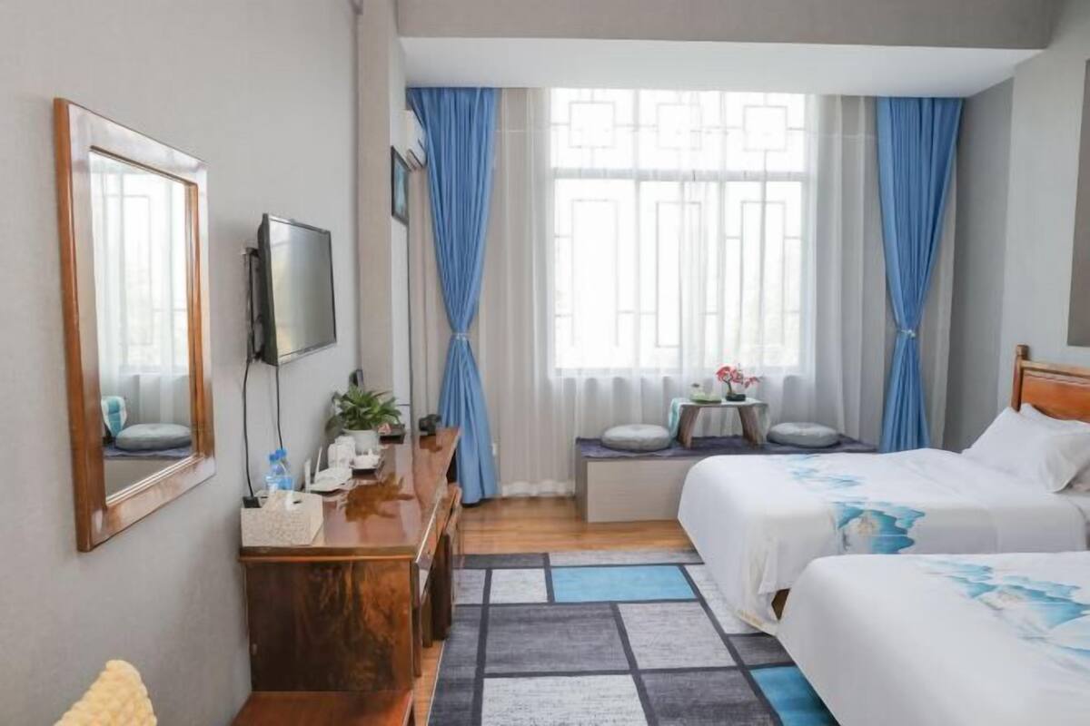 A hotel room with two beds, a desk with a chair, a TV, and a window with curtains.