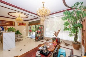 A hotel lobby with a reception desk, a chandelier, potted plants, and a large window with curtains. - Qianshuiwan Hotel (Tengchong)