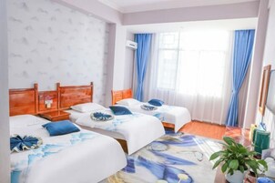 Habitación de hotel con dos camas, un ventanal grande con cortinas azules, una planta en la mesita de noche y una alfombra estampada.