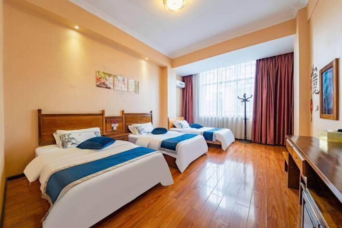 A hotel room with two beds, wooden flooring, a desk, and a window with curtains.