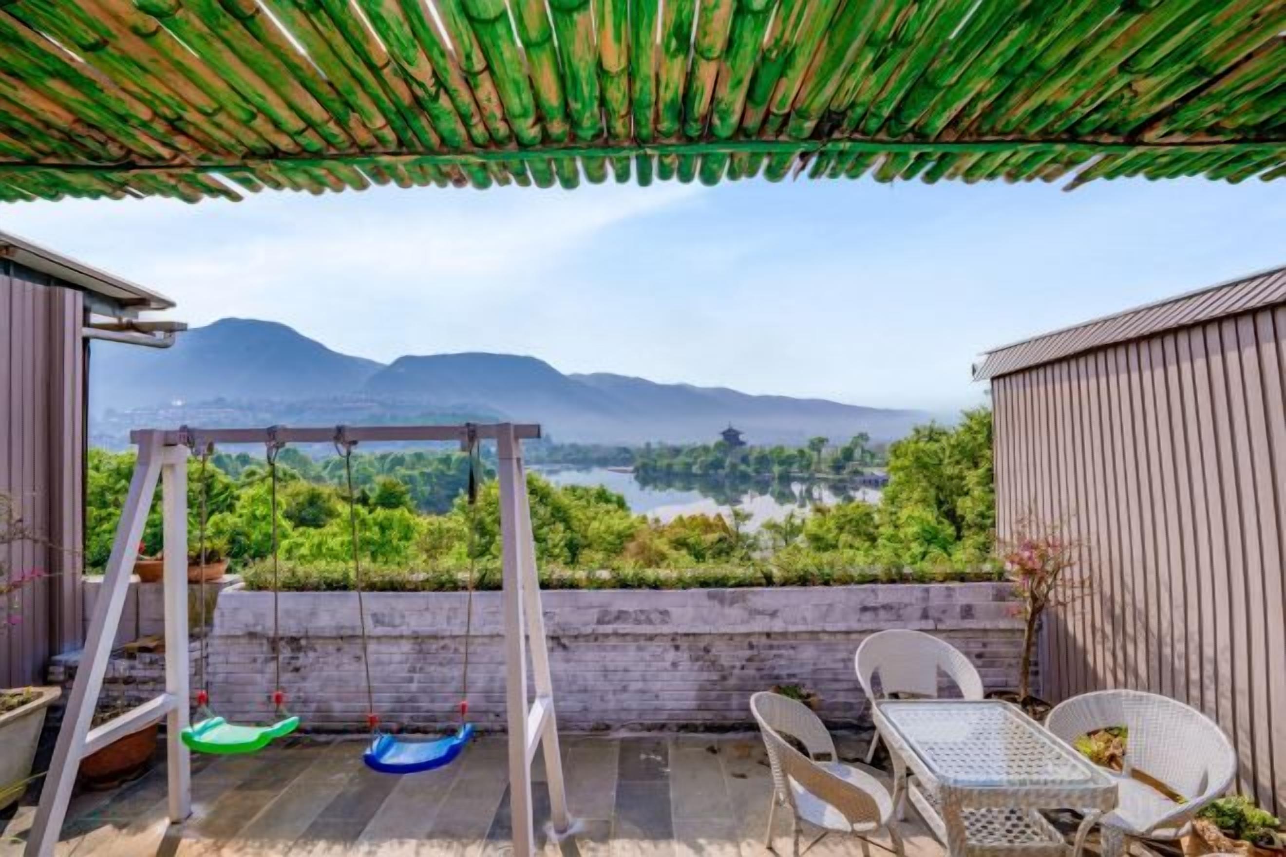 A patio with a swing set, a table, and chairs, overlooking a lake and mountains.