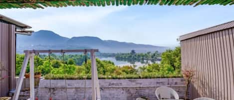 Un patio con un columpio, una mesa y sillas, con vista a un lago y montañas.