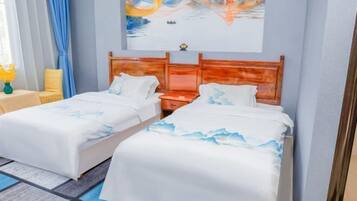 A hotel room with two beds, a wooden headboard, a painting on the wall, and a small table with a vase of flowers.