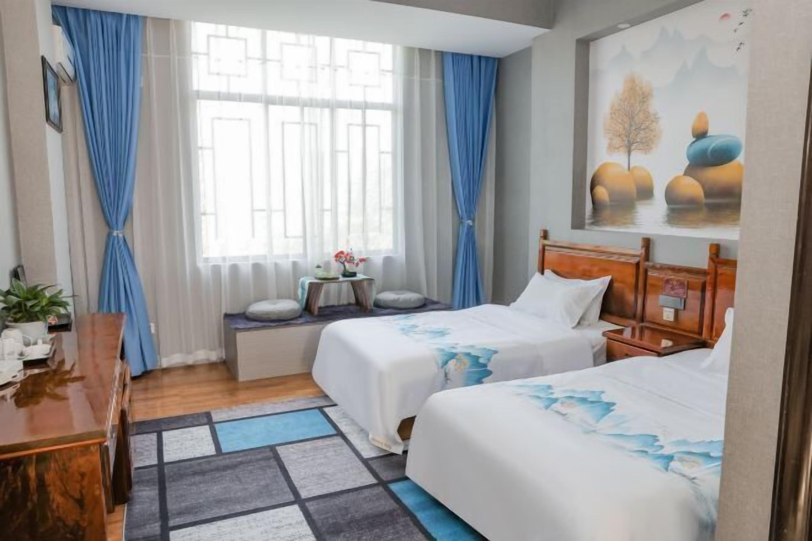 A hotel room with two beds, a desk, a small table with a plant, and a painting on the wall.