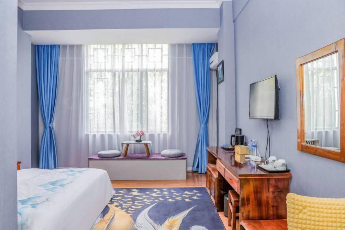 A hotel room with a bed, a desk, a chair, a TV, and a window with curtains.