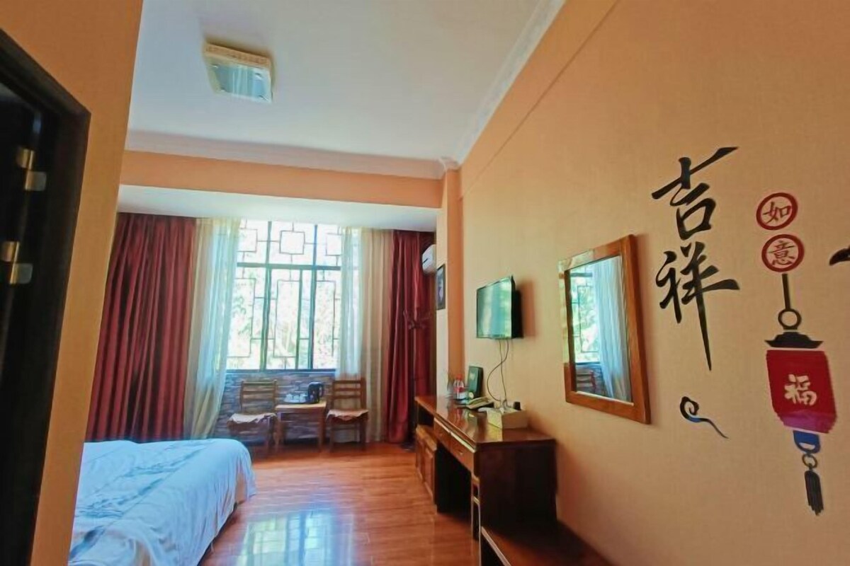 A hotel room with a bed, a desk, a chair, a TV, and a wall with Chinese characters.