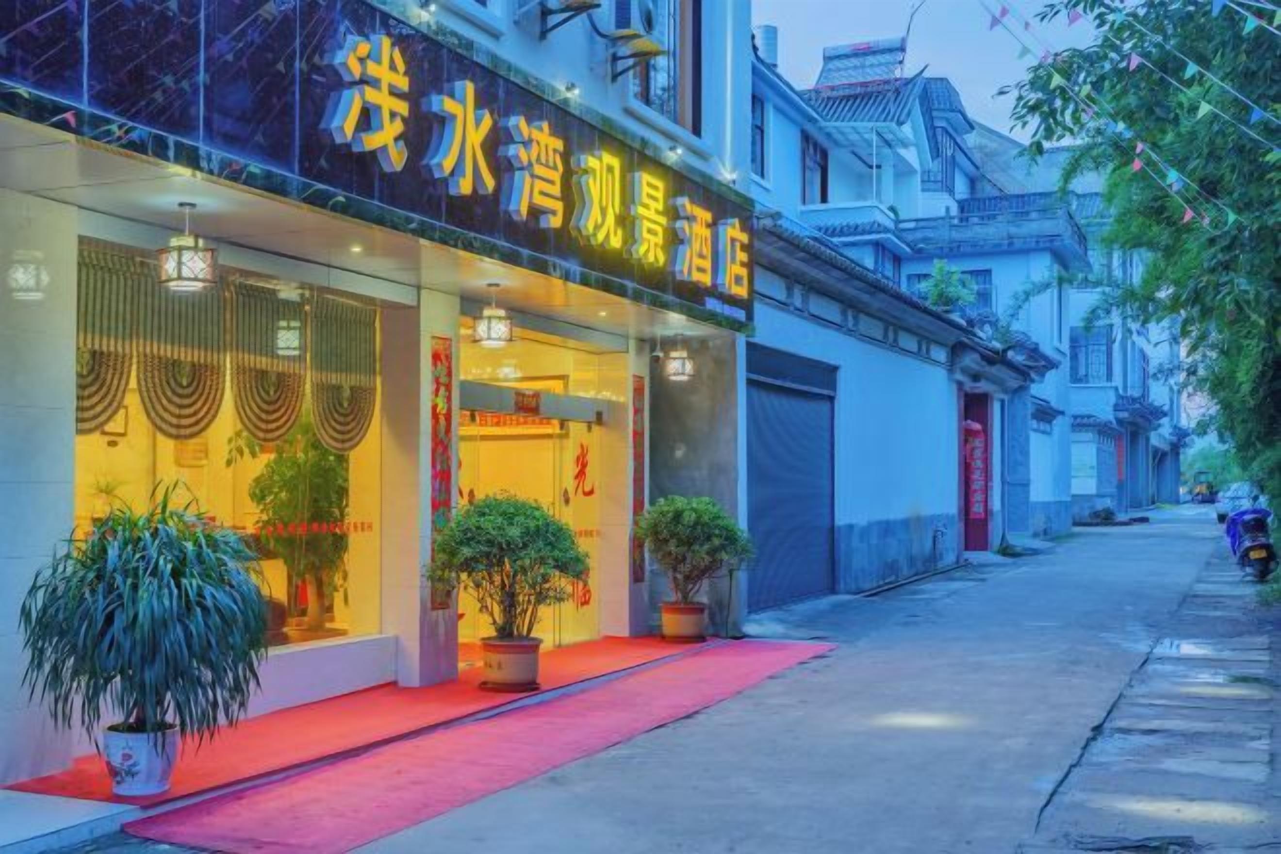 Un hotel con alfombra roja en la entrada, plantas en macetas y elementos arquitectónicos chinos tradicionales.
