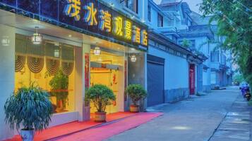 Un hotel con alfombra roja en la entrada, plantas en macetas y elementos arquitectónicos chinos tradicionales.
