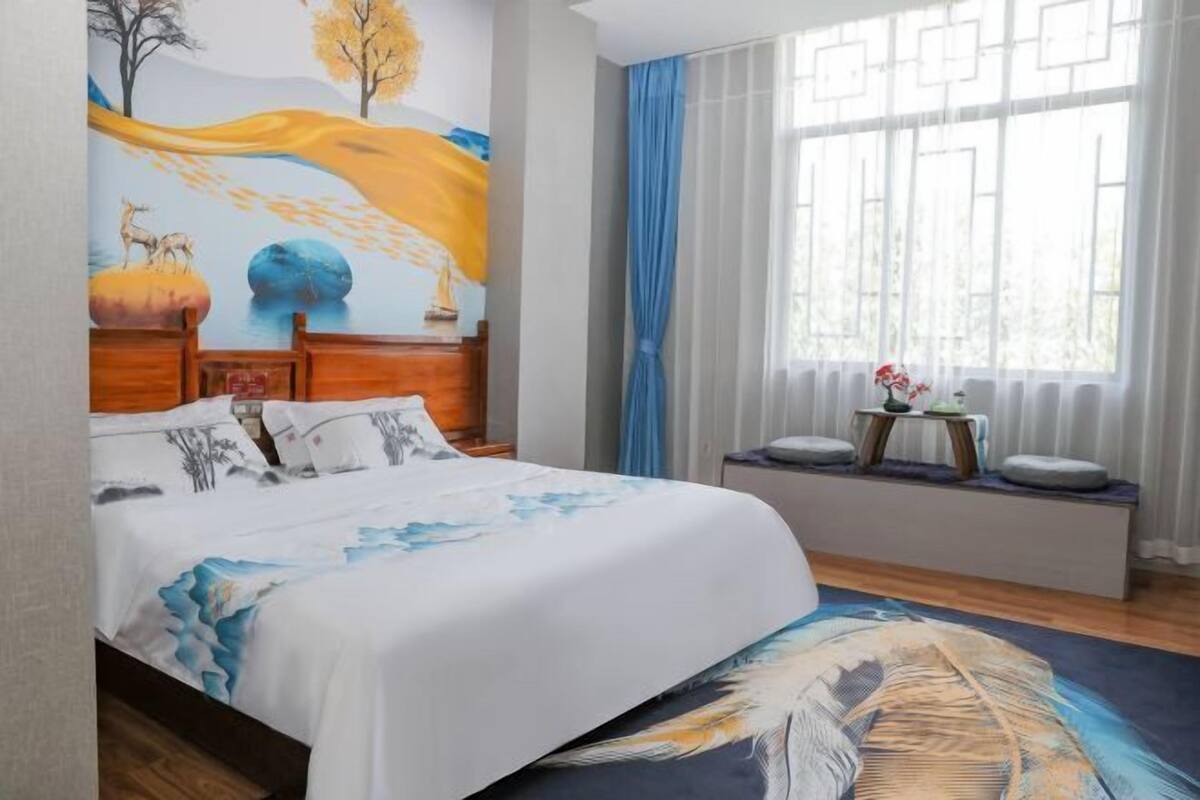A bedroom with a bed, a window with curtains, a bedside table, and a wall mural.