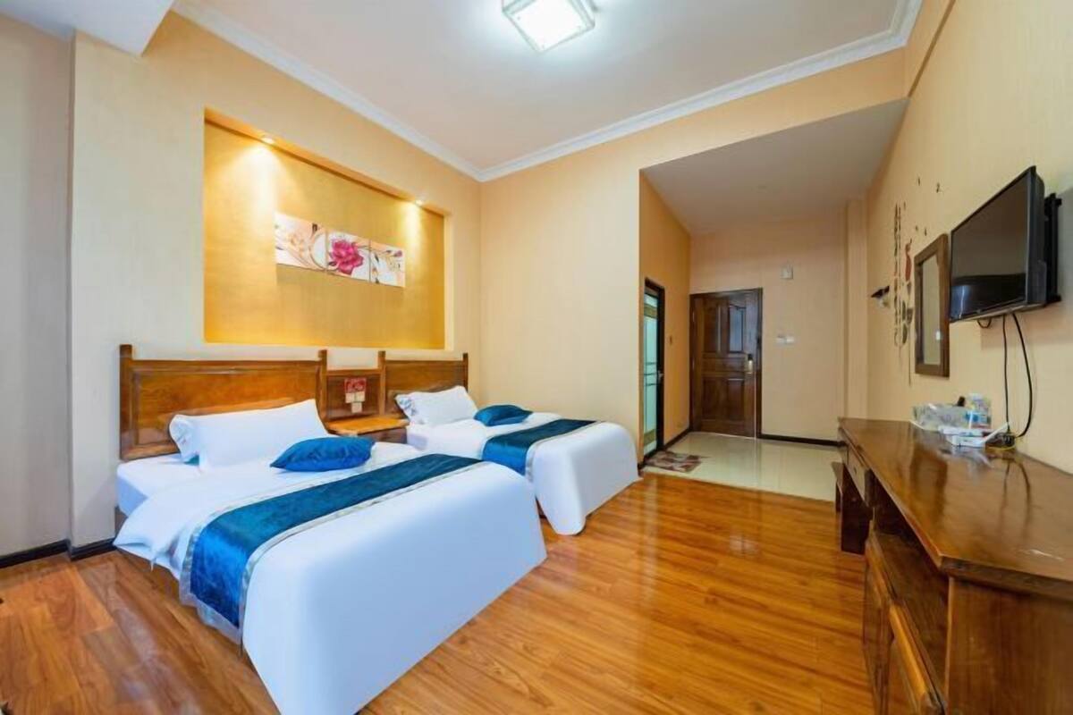 A hotel room with two beds, wooden flooring, a TV, and a painting on the wall.
