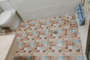 Un baño con piso de cerámica, inodoro y zona de ducha.